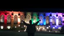 Marshaé Sylvester stands with hands raised in celebration in front of the library at Northwestern lit by rainbow colored lights shine on 