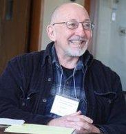 Greg seated a table, smiling, wearing a name tag.