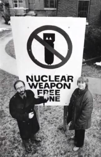 Two people stand in front of sign that says "Nuclear Weapon Free Zone."